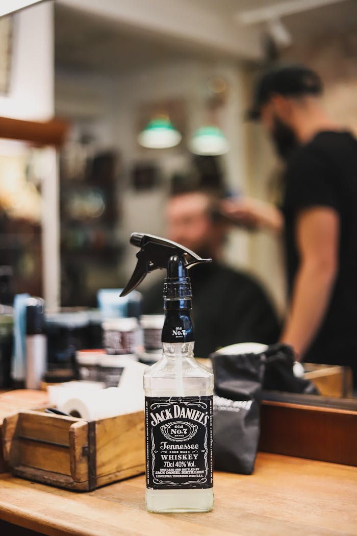 why-choose-us A Jack Daniels spray bottle in a barber shop setting with a stylist and client in the background.