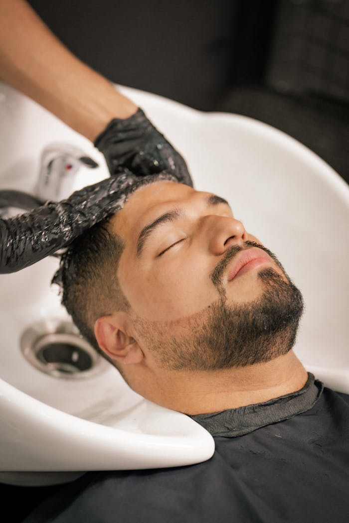 services-03 A man with closed eyes enjoys a calming hair wash at a barbershop sink.